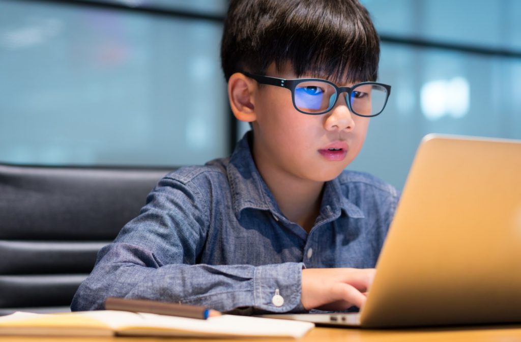 Child wearing blue light glasses as he works on his laptop.