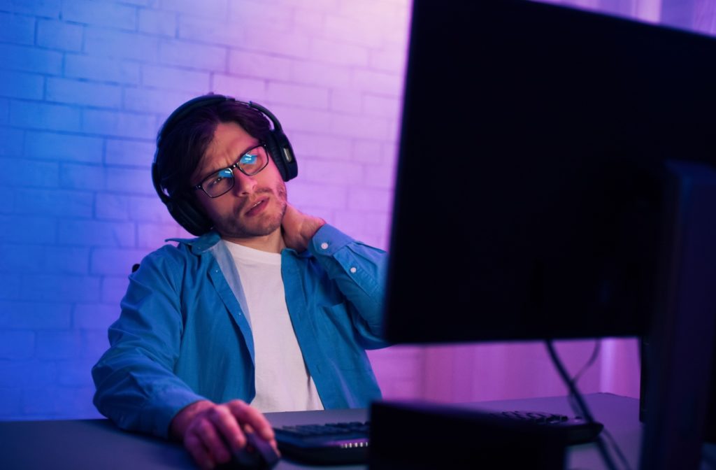 A man massages his sore neck while using his computer.