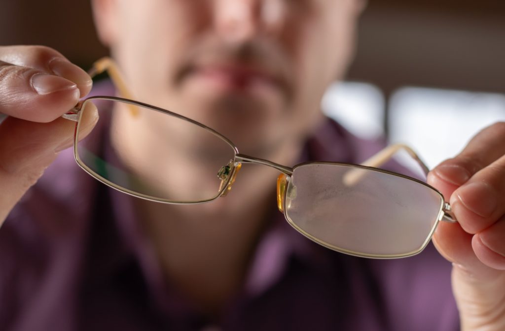 Close-up on a person holding out their glasses with a foggy lens.