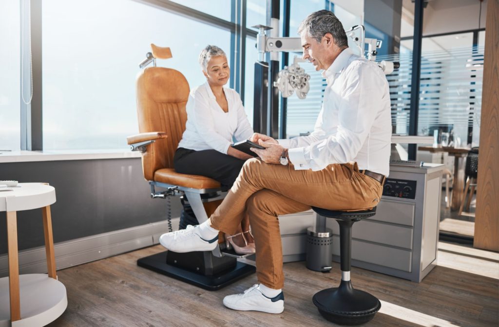 An image of an eye doctor sitting down with a patient in their office to provide guidance in terms of their eye health. The office is well-lit and sunny and the mood is positive.