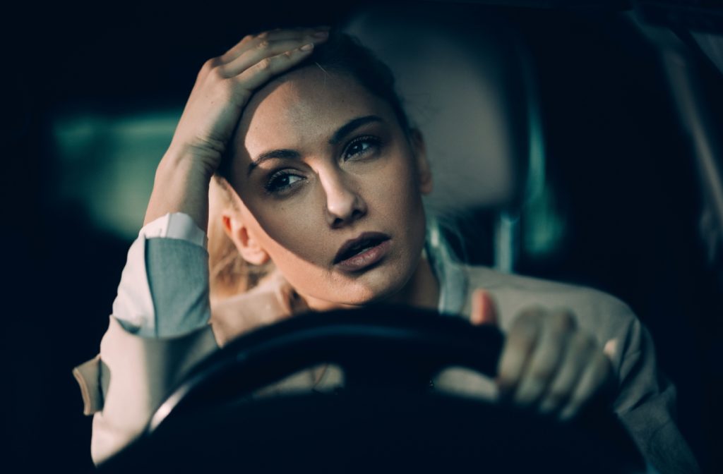 An adult in their car at night rubbing their forehead in frustration and having trouble seeing clearly due to vision problems.