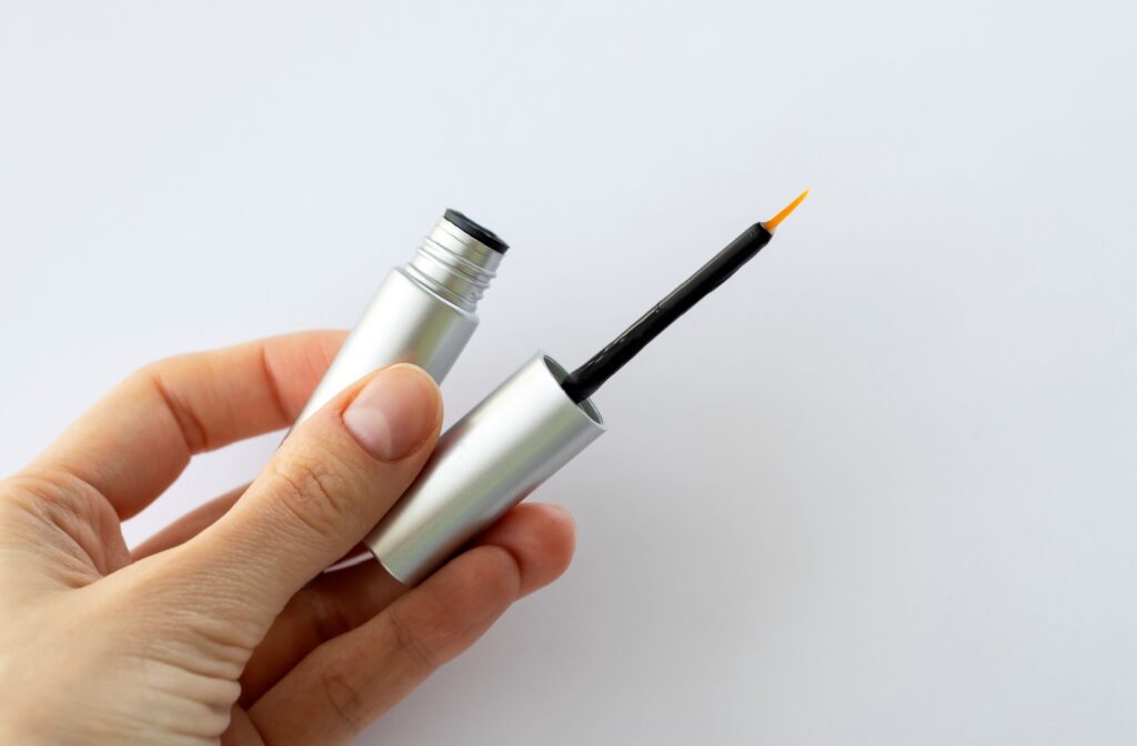 A hand holding a bottle of eyelash serum.