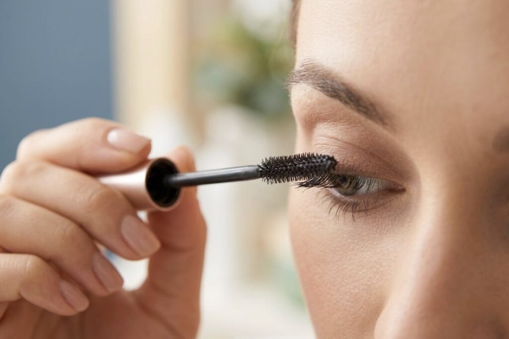 A close up of a mascara wand swiping mascara onto eyelashes.