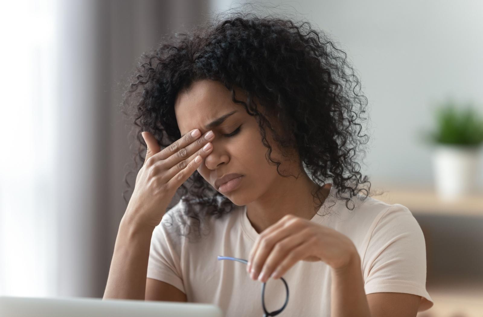 A person holding glasses in one hand and holding their head with the other hand due to eye strain from wearing the incorrect glasses prescription.